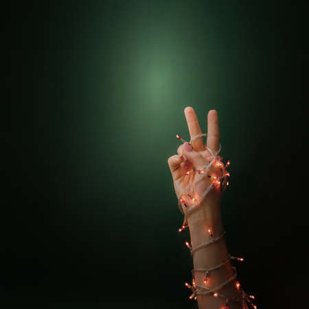 Beautiful female hand wrapped with new year Christmas red lights with two fingers on green dark...