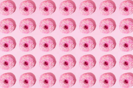 Arranged pink ring donuts whith glaze and white crumbs on a pink pastel background. Pattern. Flat lay.の写真素材