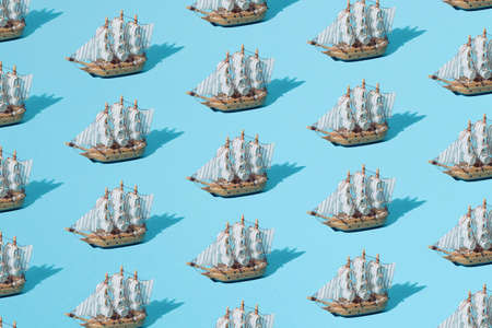 Small wooden home decoration pirate ship with white sails on a blue pastel background. Pattern. Minimal concept and design.の写真素材