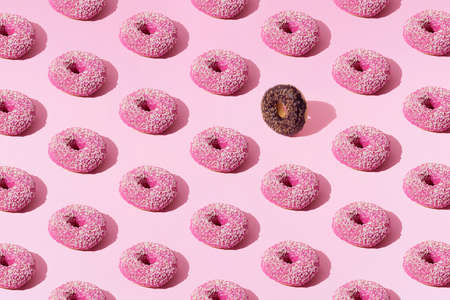 Arranged small pink and chocolate ring donuts whith pink and chocolate glaze and white and brown crumbs on a pink pastel background. Pattern.の写真素材
