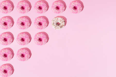 Arranged pink and white ring donuts like triangle whith glaze and colorful crumbs on a pink pastel background. Pattern. Copy space.の写真素材