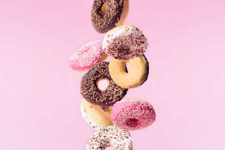 Falling ring donuts with white, pink and chocolate glaze. Colorful crumbs on a pink pastel...