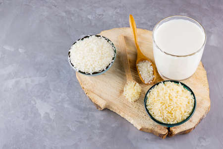 Rice milk and rice seeds on a gray background. Rice milk in glass on a wooden stand. Vegan non-dairy...