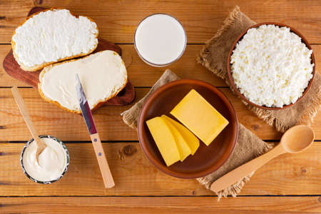 Various dairy products. Milk, cottage cheese, hard cheese and sour cream in a rustic style. Bread with cream cheese on a wooden boards. Top viewの写真素材