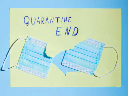 Surgical mask in a paper hole. COVID-19 protection Concept. Protective face mask and a torn yellow paper. Inscription "Quarantine End". Quarantine Completionの写真素材