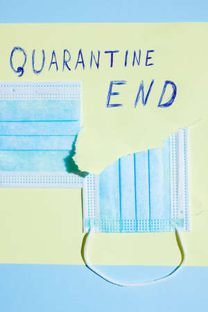 Surgical mask in a paper hole. COVID-19 protection Concept. Protective face mask and a torn yellow paper. Inscription "Quarantine End". Quarantine Completionの写真素材