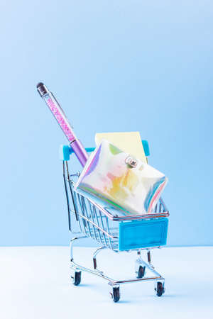 Shopping cart with school supply. School notepad with holographic cover. Stationery in shopping trolley. Back to school conceptの写真素材