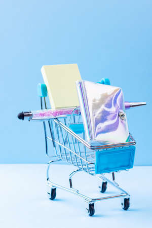 Shopping cart with school supply. School notepad with holographic cover. Stationery in shopping trolley. Back to school conceptの写真素材