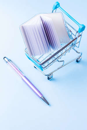 Shopping cart with school supply. School notepad with holographic cover. Notepad and pen in shopping trolley. Back to school conceptの写真素材