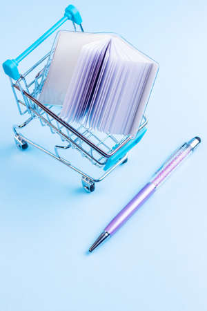 Shopping cart with school supply. School notepad with holographic cover. Notepad and pen in shopping trolley. Back to school conceptの写真素材