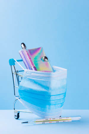 Shopping cart with protective medical mask. Thermometer, pen and notepad on shopping trolley. Safe shopping in the supermarket. Quarantine concept. Copy spaceの写真素材