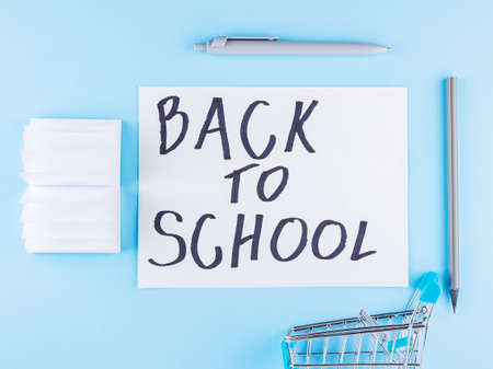 Back to school concept. Shopping cart and stationery on blue background. Pen, pencil and notepad for school. Top viewの写真素材
