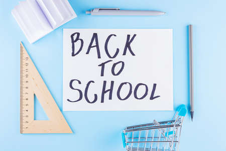 Back to school concept. Shopping cart and stationery on blue background. Pen, triangle and notepad...