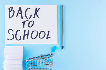 Back to school concept. Shopping cart and stationery on blue background. Pen, pencil and notepad for school. Top viewの写真素材
