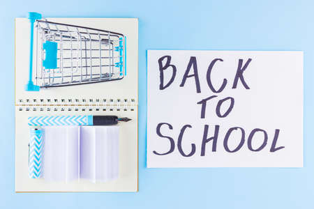 Back to school concept. Shopping cart and stationery on blue background. Pen, notepad and shopping trolley. Time to study. Top viewの写真素材