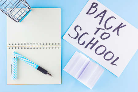 Back to school concept. Shopping cart and stationery on blue background. Pen, notepad and shopping trolley. Time to study. Top viewの写真素材