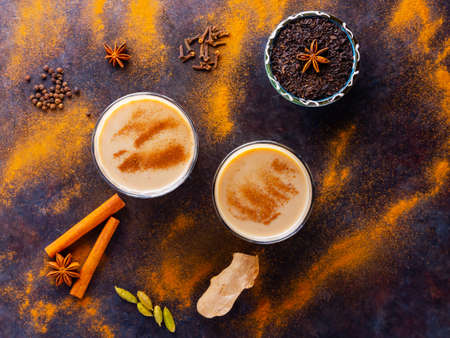 Masala chai tea on a black background. Two transparent glasses of masala tea and scattered various...