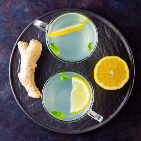 Ginger tea with lemon on a dark background. Two cups of ginger tea on a black plateの写真素材