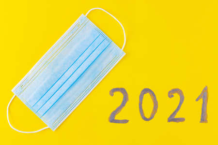 Text 2021 on a yellow background and surgical mask. Concept of the New Year with blue protective...