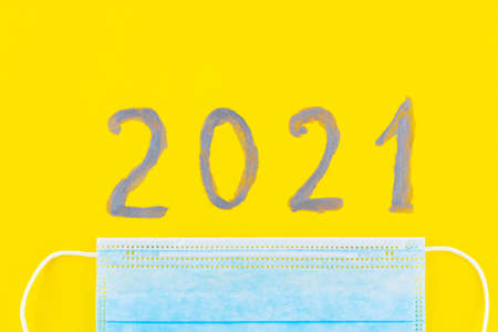 Text 2021 on a yellow background and surgical mask. Concept of the New Year with blue protective mask. Celebrating New Year in quarantine, covid-19, coronavirus. Top viewの写真素材