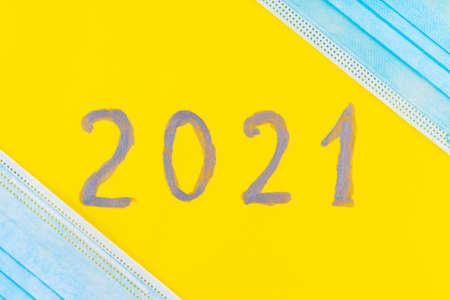 Text 2021 on a yellow background and surgical mask. Concept of the New Year with blue protective mask. Celebrating New Year in quarantine, covid-19, coronavirus. Top viewの写真素材