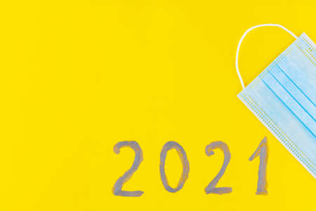 Text 2021 on a yellow background and surgical mask. Concept of the New Year with blue protective...