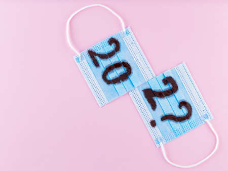 Text 202? on pink background and surgical mask. Concept of the New Year with blue protective mask....