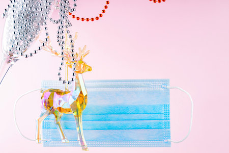 Toy deer and a glass with christmas beads on a pink background. New Year medical concept with holographic deer and protective face mask. Pandemic Christmas concept. Levitationの写真素材