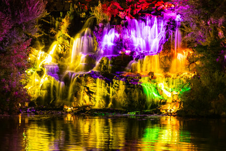 Waterfall in neon color. Flowing water illuminated by multicolored light. Night landscape with a colorful waterfall near the riverの写真素材