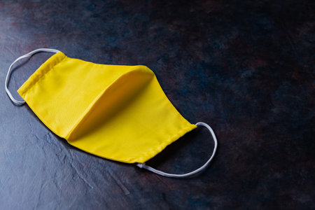 Face protective mask. Reusable antivirus mask made from yellow cotton. Yellow protective mask on a dark background. Eco-friendly tailoring. Top view. Copy spaceの写真素材