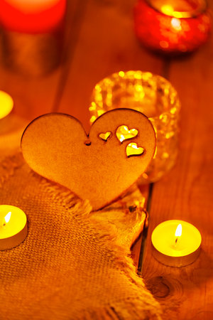 Wooden heart and candles on burlap and wooden boards. St Valentine's day greeting card with candle and heart on a blurred background. Love story concept. Copy spaceの写真素材