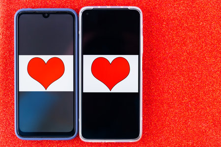 Online dating concept. Red hearts on the two smartphones screens. Valentine's Day concept on a red glitter background. Copy space. Top viewの写真素材