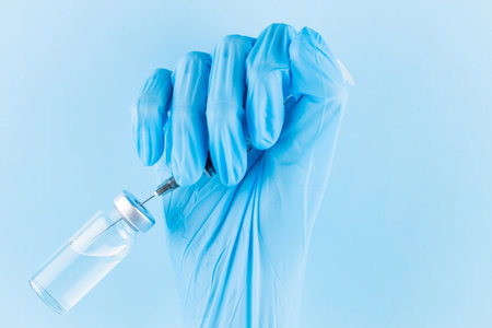 Hand filling syringe with medication. Robotic arm in surgical glove holding syringe with Covid-19 vaccine. Vaccination and immunization concept. Copy spaceの写真素材