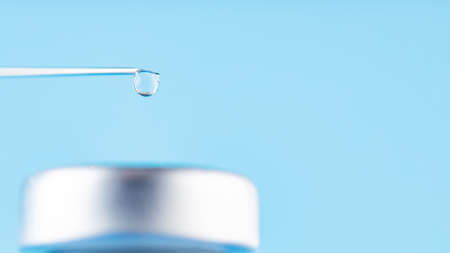 Vaccine drop on syringe needle. Vaccination concept, disease prevention. Needle with a drop of vaccine on a blue background.の写真素材