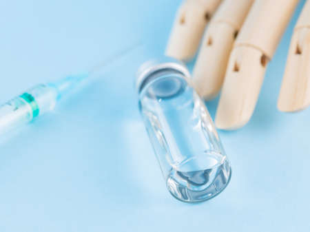 Vaccine, syringe and wooden human hand. Medical ampoule and syringe on blue background. Health care...