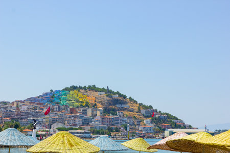 Kusadasi, Turkey - July 29, 2019: Beach umbrellas and view of Kusadasi. Turkish resort town, view of colorful houses. Summer vacation conceptのeditorial素材