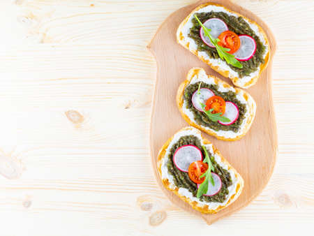 Vegan sandwiches with avocado cream on a cutting board. Healthy sandwiches with cream cheese, avocado, radish, cherry tomatoes and arugula. Top view. Copy spaceの写真素材