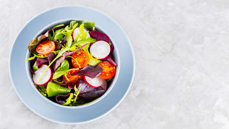 Healthy vegetable salad with cherry tomatoes, radish and mix salad. Vegan salad with mix of greens on gray background. Paleo diet concept. Copy space. Top viewの写真素材