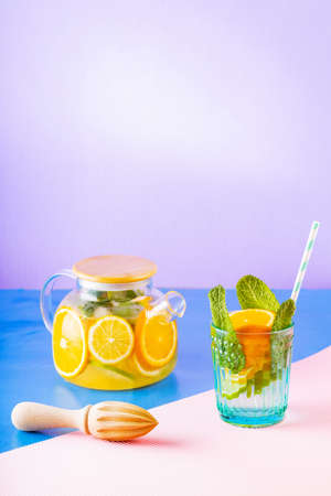 Lemonade drink of water, lemon, orange and mint leaves on multicolored background. Lime mint iced...