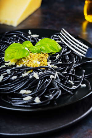 Black spaghetti with pesto sauce, basil and parmesan cheese. Black pasta with cuttlefish ink on a black plate. Traditional italian cuisineの写真素材