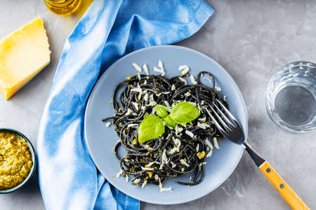 Black spaghetti with cuttlefish ink on a gray background. Black pasta with parmesan cheese, basil and pesto sauce. Pasta with grated cheese and ingredients. Top viewの写真素材