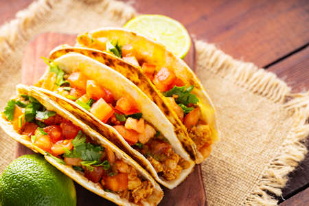 Taco with meat and vegetables on sackcloth. Mexican tacos and limes on wooden boards. Taco with meat, tomatoes and herbs. Rustic style. Close-upの写真素材