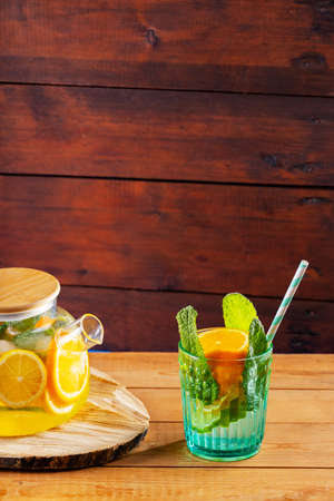 Lime mint iced tea in a transparent teapot. Lemonade drink of water, lemon, orange and mint leaves on wooden boards. Copy spaceの写真素材