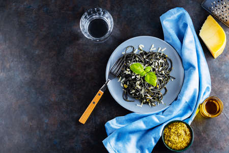 Black pasta with cuttlefish ink on a gray plate. Black spaghetti with parmesan cheese, basil and pesto sauce. Pasta with grated cheese and ingredients. Top view. Copy spaceの写真素材