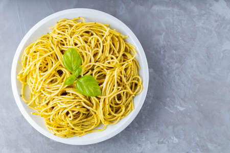 Pasta with sauce pesto and basil leaves on a white plate. Spaghetti with pesto sauce and fresh basil on a gray background. Copy space. Top viewの写真素材