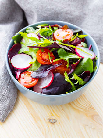 Healthy salad with cherry tomatoes, radish and mix salad. Salad with mix of greens on wooden background. Copy spaceの写真素材