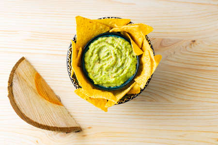 Guacamole sauce with corn chips on wooden background. Tortilla chips and Mexican guacamole sauce in...