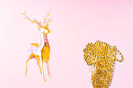 Toy deer and Christmas beads in a champagne glass on a pink background. Christmas composition with holographic toy deer. Festive holiday concept. Copy spaceの写真素材