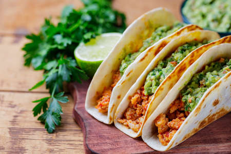 Tacos with fried minced meat and guacamole sauce on a wooden boards. Mexican tacos, cilantro and lime on wooden background. Mexican cuisine. Rustic styleの写真素材