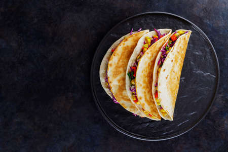 Vegetarian tacos with sweet corn, purple cabbage and tomatoes on a black plate. Tacos with...
